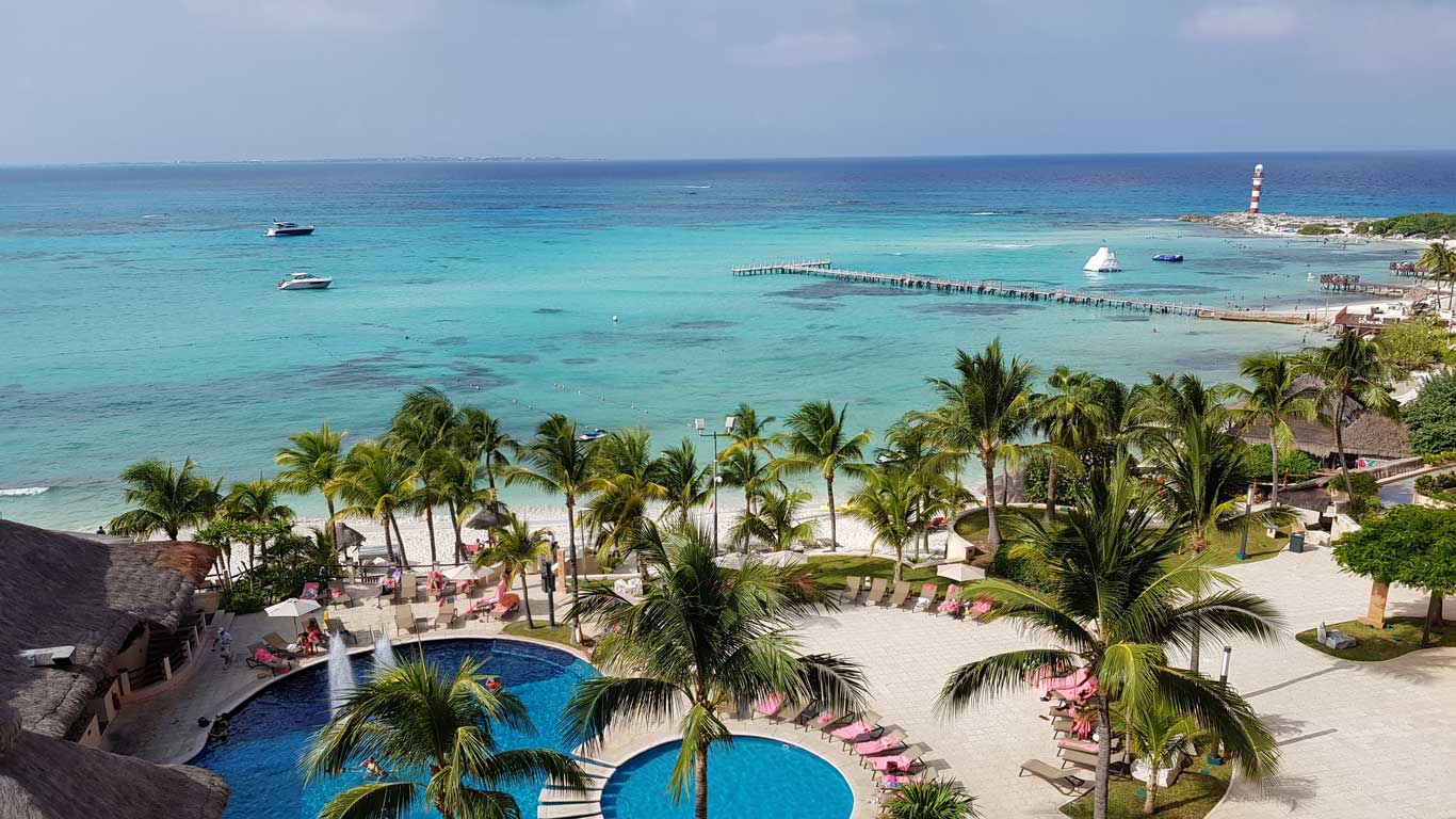 La imagen muestra una vista aérea de una playa en Cancún, México, con aguas cristalinas de tonos turquesa y varios yates flotando cerca de la costa. Eso es uno de los mejores destinos para viajar con amigos.