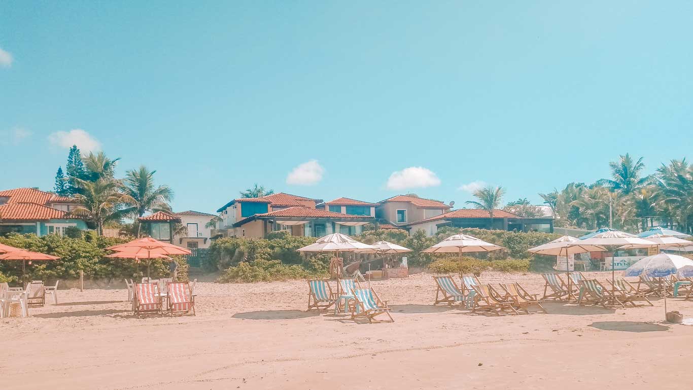 Una escena de la Playa de Geribá, una excelente opción de dónde alojarse en Búzios, con varias sillas en la arena de la playa y casas al fondo.