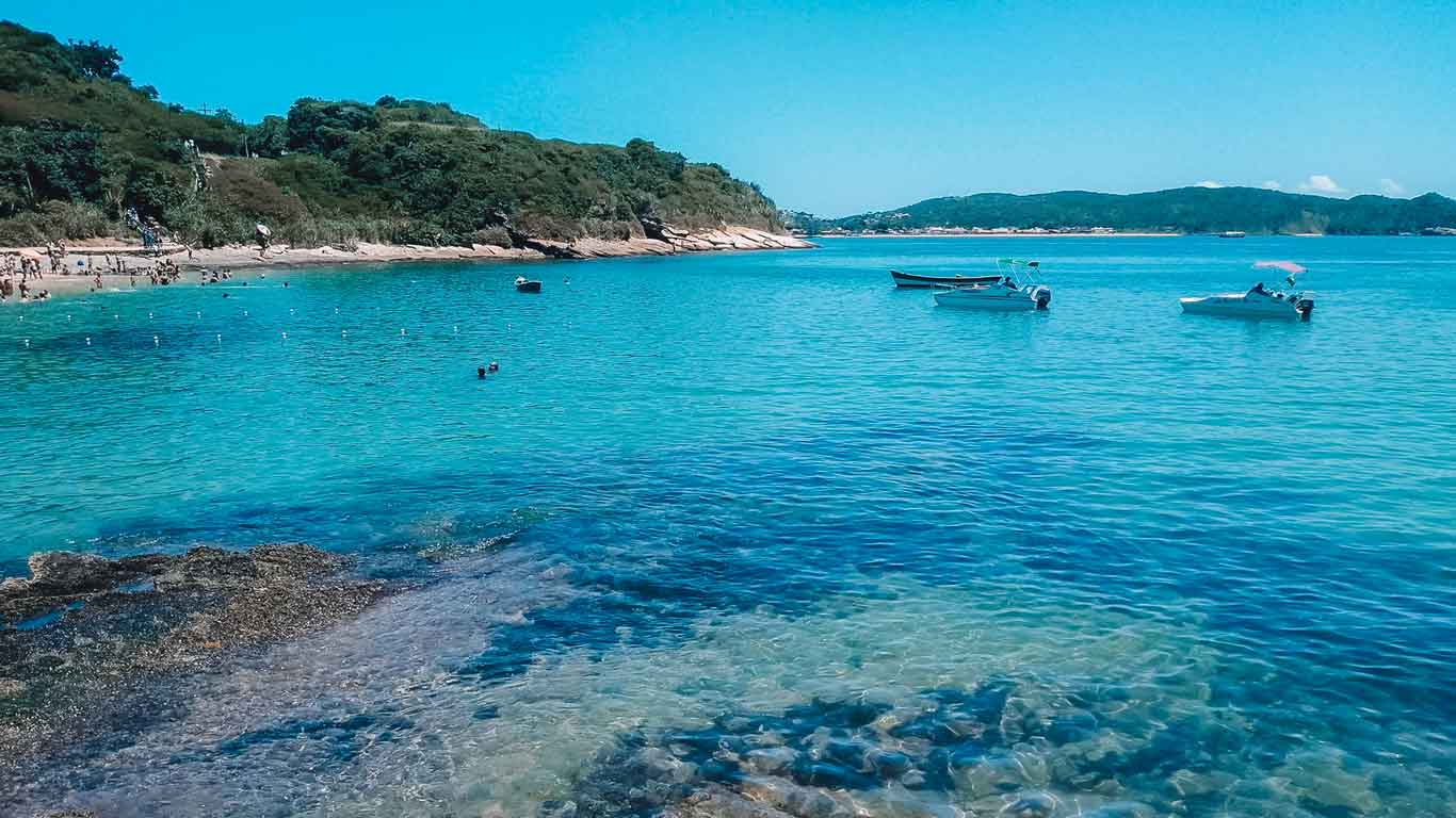 Imagen de la Playa de João Fernandes en Búzios, con aguas transparentes y algunos barcos al fondo.