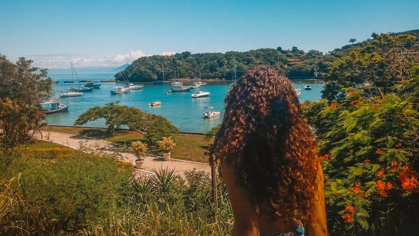 Una mujer de cabello ondulado admirando la Playa dos Ossos desde lo alto, uno de los mejores lugares para hospedarse en Búzios.