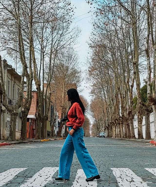 Mujer con una sudadera roja cruzando una calle de Colonia del Sacramento, en un día tranquilo.