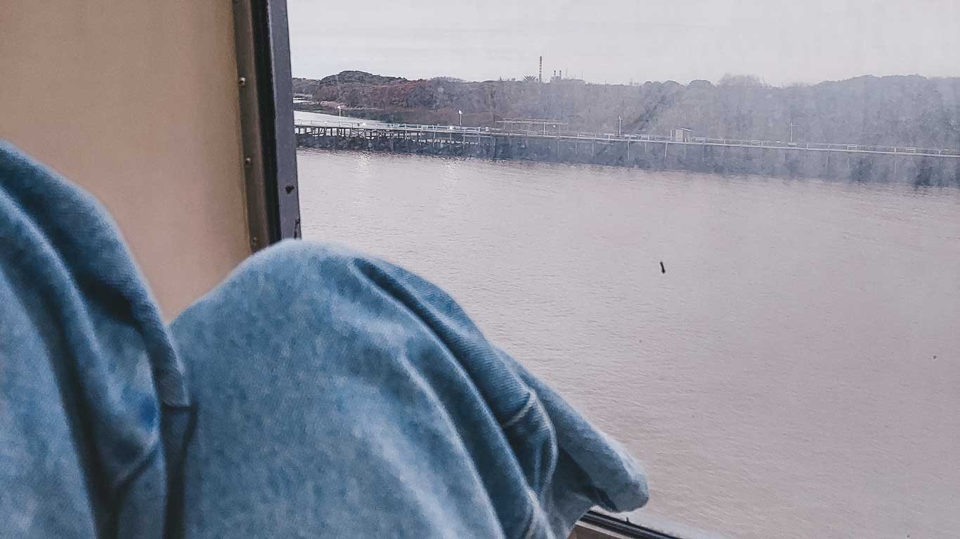 Imagen de las piernas de una mujer sentada en la ventana del ferry de Buenos Aires a Colonia del Sacramento.