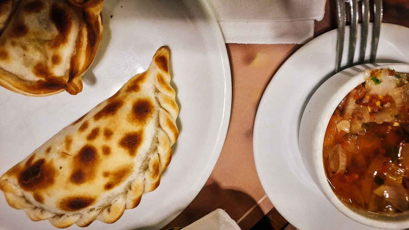 Imagen de dos empanadas uruguayas horneadas acompañadas de salsa.