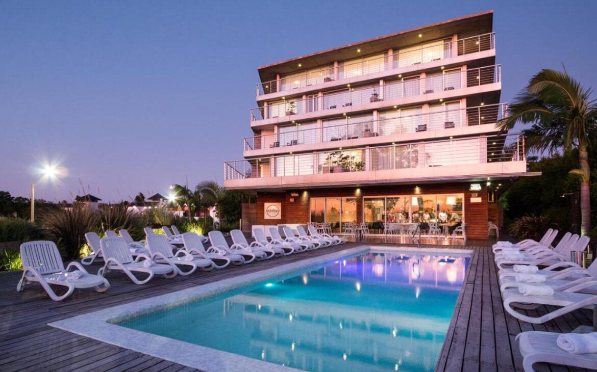 El crepúsculo cae sobre el Costa Colonia Boutique Hotel, con su moderna arquitectura de varios pisos que presenta balcones con vistas a una serena zona de piscina alineada con tumbonas blancas, acentuada por el suave resplandor de las luces junto a la piscina y un ambiente tranquilo.