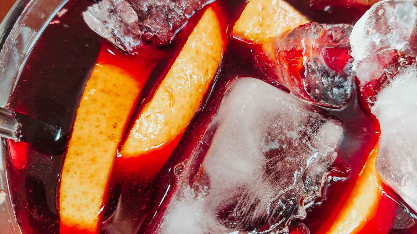 Foto de sangría con trozos de naranja, hielo y vino.