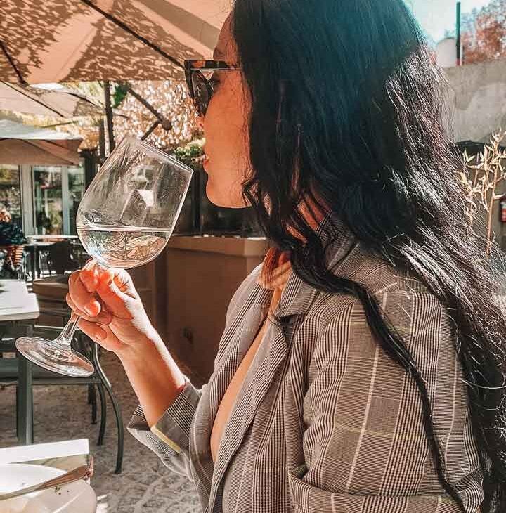 Una mujer disfrutando de una copa de vino blanco, iluminada por los rayos del sol.
