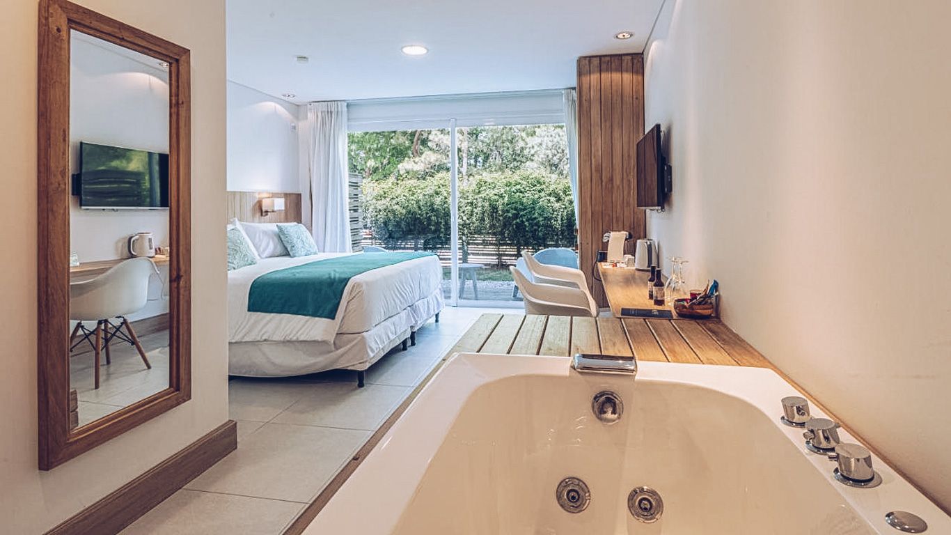 La fotografía muestra una elegante habitación del Live Hotel Boutique en Punta del Este. Esta suite combina un diseño contemporáneo con comodidad, destacando una amplia bañera de hidromasaje en primer plano, integrada armónicamente con el espacio de la habitación.