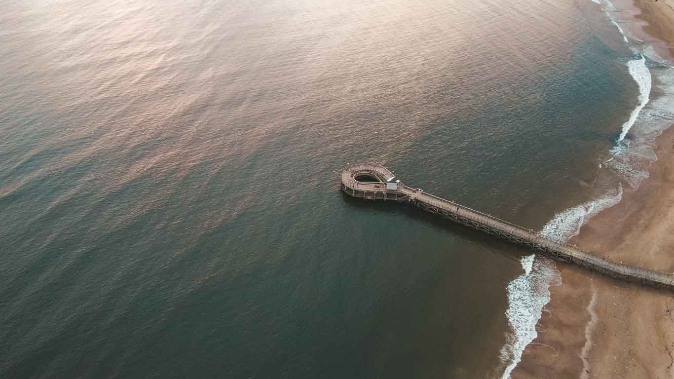 La imagen captura una vista aérea de un muelle en espiral que se adentra en las tranquilas aguas de la Playa Mansa en Punta del Este. Desde esta perspectiva, se observa la serenidad del mar y la suave arena de la playa que define esta popular zona costera. La estructura del muelle, única por su forma circular, ofrece un punto de vista privilegiado sobre el océano.