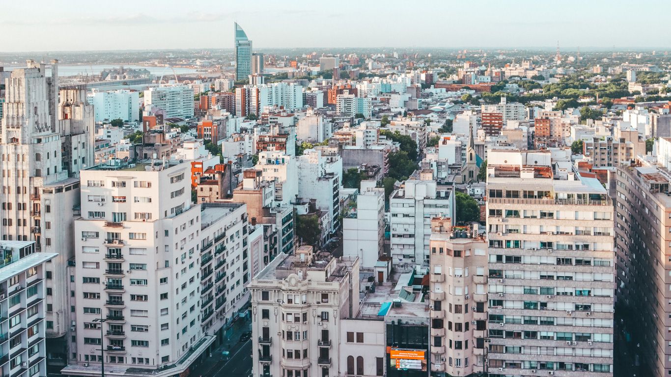 Vista panorámica de Montevideo, mostrando una variedad de edificios residenciales y comerciales bajo un cielo despejado. En el fondo, se puede ver el distintivo World Trade Center Montevideo y el puerto de la ciudad.