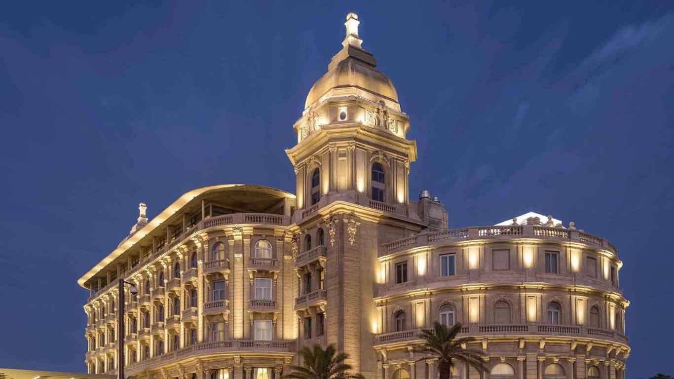 La imagen muestra el elegante edificio del Sofitel Montevideo Casino, iluminado por luces cálidas contra un cielo nocturno. La arquitectura clásica y majestuosa del hotel se destaca, con detalles ornamentales y una gran cúpula. El ambiente lujoso del Sofitel Montevideo Casino resplandece en la noche, mostrando su impresionante presencia en la ciudad.