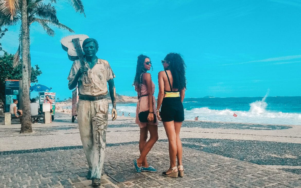 Chicas junto a la estatua de Tom Jobim en la Playa de Ipanema, una excelente opción dónde alojarse en Río de Janeiro.