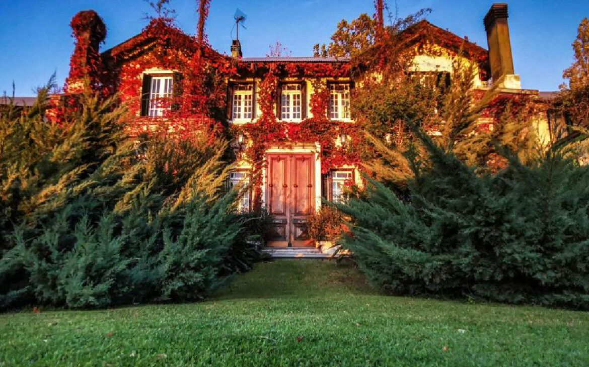 Fotografía de la fachada de La Casa de Los Limoneros, destacándose por sus tonos rojos entre los arbustos circundantes.