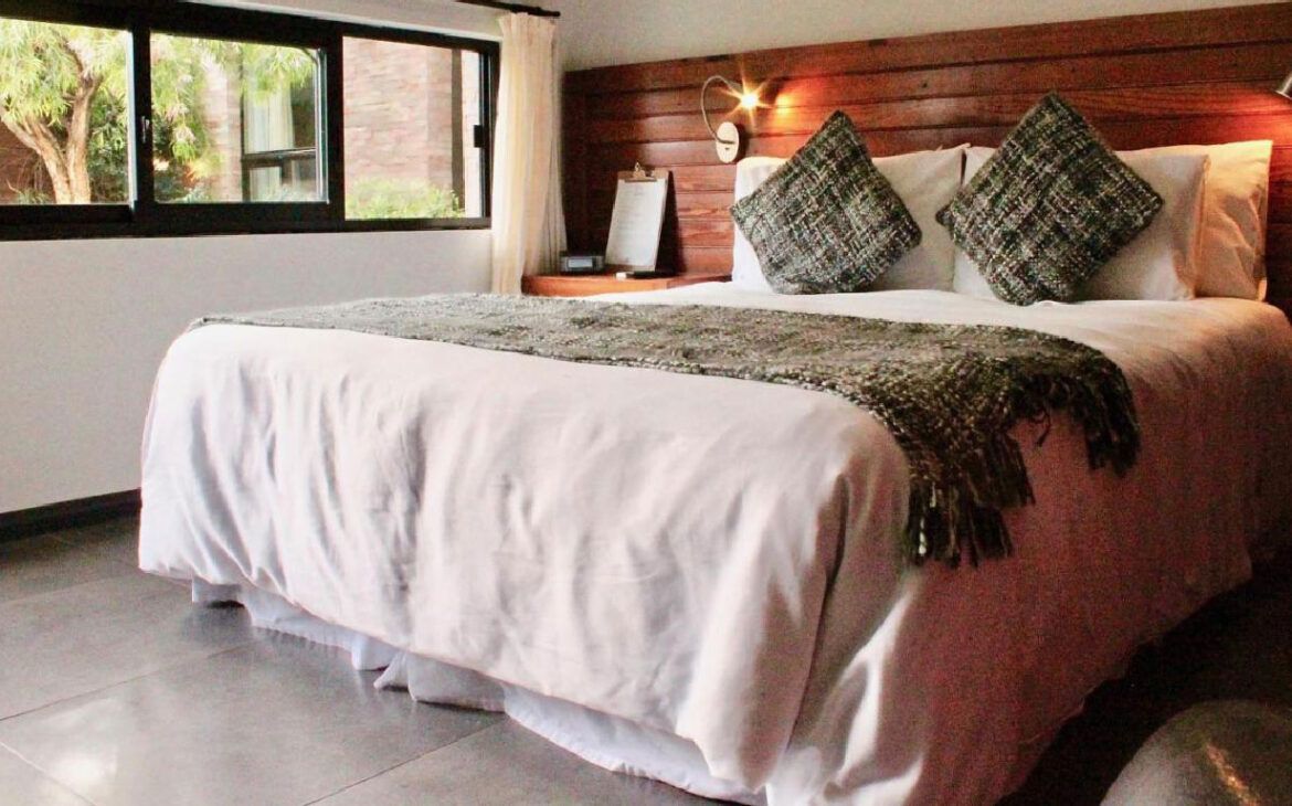 Habitación de la Posada Boutique Las Terrazas en Colonia del Sacramento con detalles de madera y una cama doble con sábanas blancas.