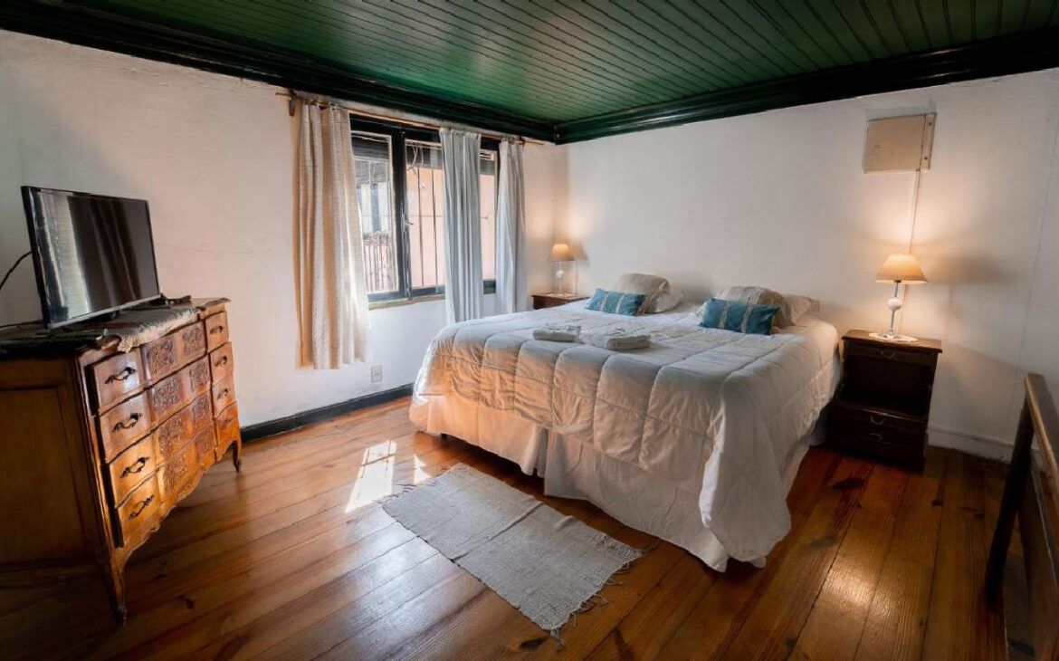 Una habitación modesta en la Posada de la Flor en Colonia del Sacramento, caracterizada por muebles antiguos y una cama con sábanas blancas.
