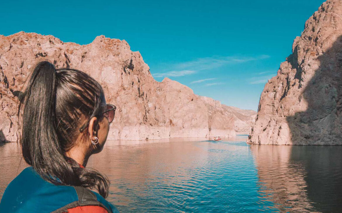 Mujer con el cabello oscuro recogido y gafas de sol, contemplando los paisajes del Cañón del Atuel durante un paseo en barco, donde las rocas y las aguas azules se fusionan en un paisaje deslumbrante.