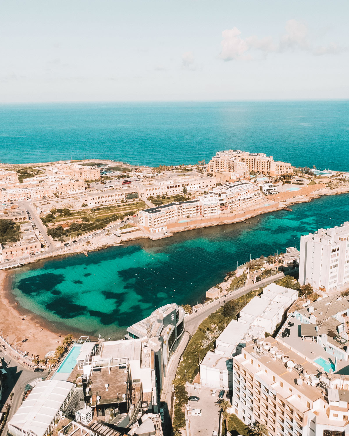 Vista aérea de St. Julian's, la mejor zona para hospedarse en Malta, mostrando las aguas turquesas claras de la bahía, la arquitectura mediterránea circundante y el paisaje urbano.