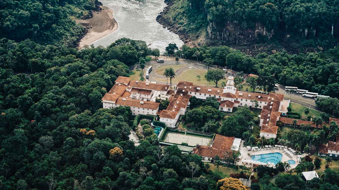 Vista aérea del Hotel das Cataratas, el mejor hotel donde alojarse en las Cataratas del Iguazú del lado brasileño, rodeado por la selva con las aguas de la catarata frente a él, donde un pequeño bote navega.