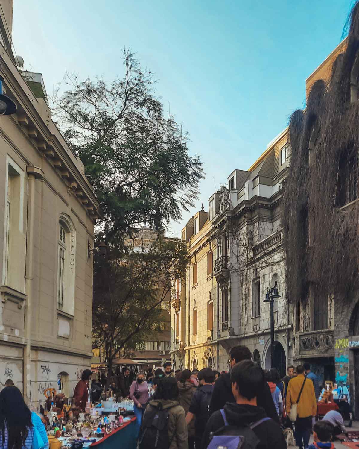 Una calle concurrida en el barrio Lastarria, la mejor zona para hospedarse en Santiago de Chile, con varias personas caminando y puestos de venta al aire libre que exhiben diversos artículos