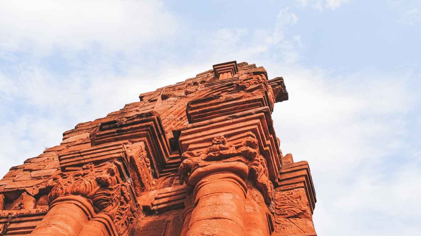 Vista en ángulo de una imponente estructura de piedra roja en las ruinas de San Ignacio Miní, Misiones, Argentina. La imagen resalta los detalles arquitectónicos tallados y la majestuosidad de la construcción contra un cielo parcialmente nublado.