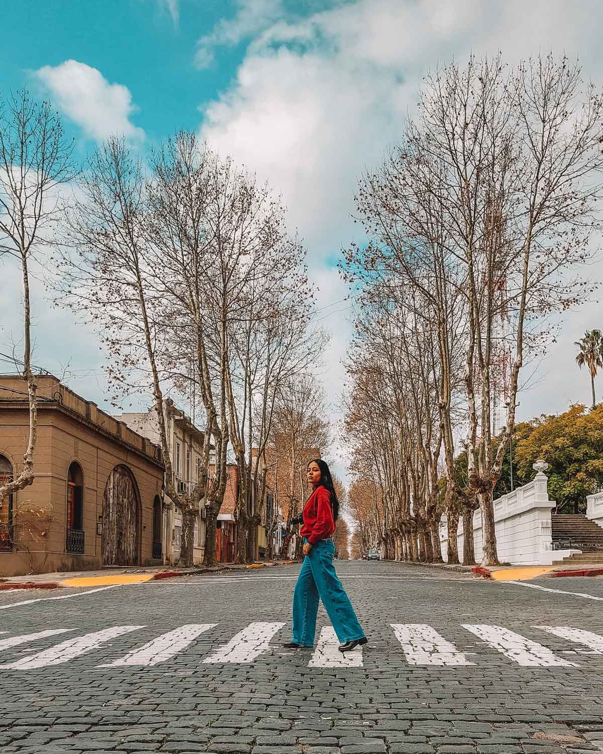 Mujer con una sudadera roja cruzando una calle de Colonia del Sacramento, en un día tranquilo.