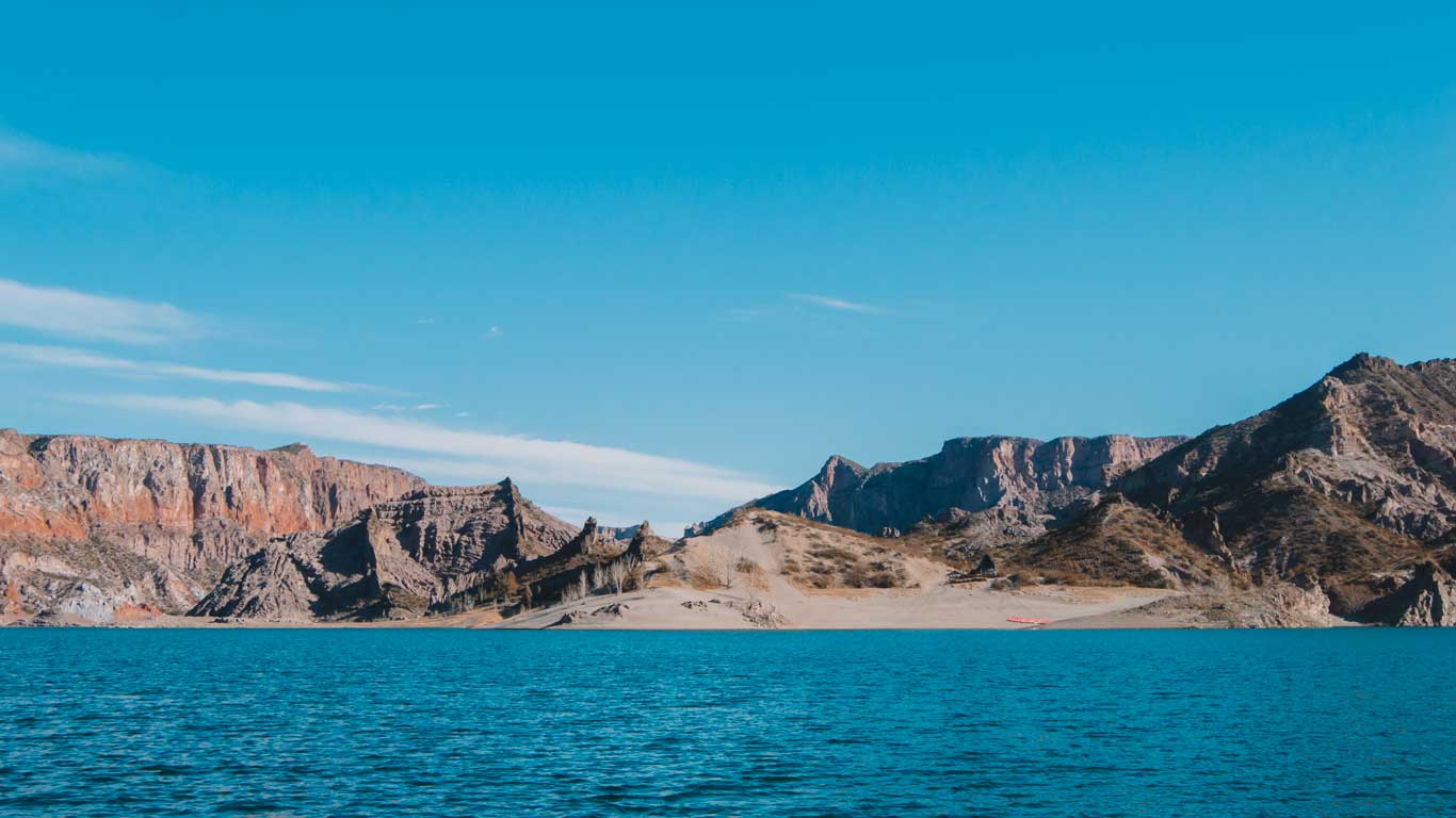 Paisaje del Cañón del Atuel, rodeado de formaciones rocosas en San Rafael, Mendoza, con montañas al fondo y un cielo azul claro.