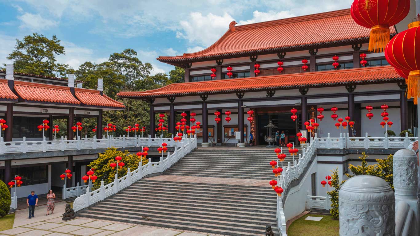 El templo Zu Lai en São Paulo, que presenta una arquitectura tradicional china con techos de tejas rojas, faroles rojos e intrincadas barandillas blancas, rodeado de exuberante vegetación. Visitar este tranquilo templo budista es una de las cosas más pacíficas y culturales que se pueden hacer en São Paulo.