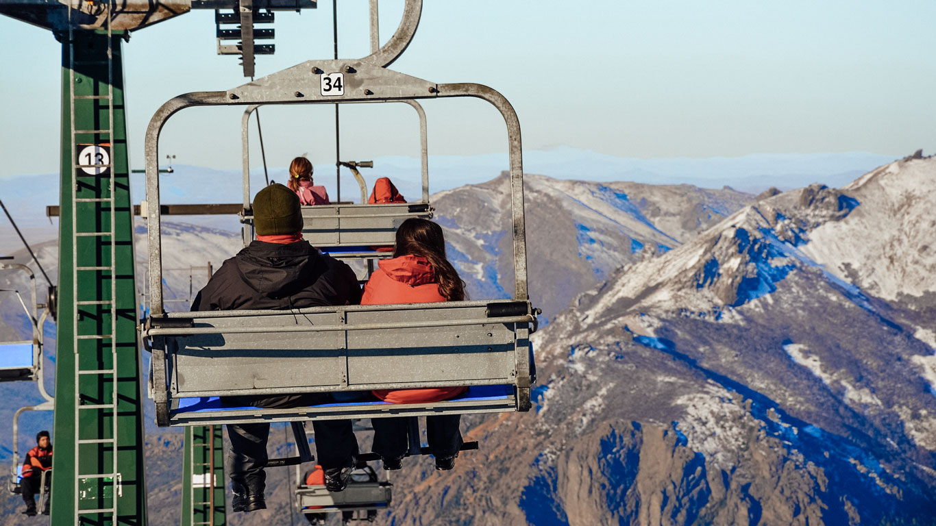 bariloche-en-el-invierno-ropas Personas subiendo en telesilla entre montañas nevadas, con vistas espectaculares de la cordillera. Escena típica de quienes disfrutan la nieve en Bariloche en temporada de esquí.