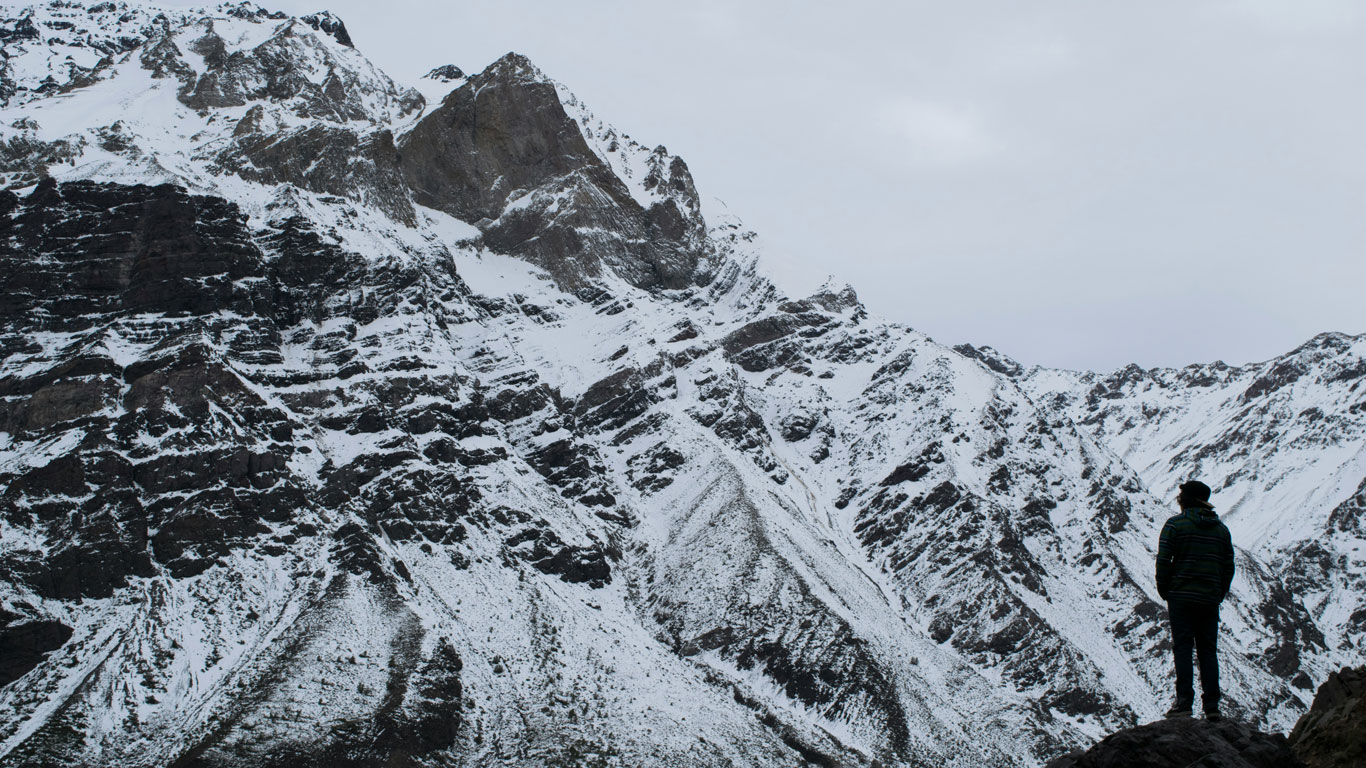 cajon-del-maipo-chile Excursionista contempla una montaña nevada en el Cajón del Maipo, uno de los destinos favoritos para ver nieve en Santiago. Las texturas de la roca y el manto blanco crean un paisaje de aventura natural.