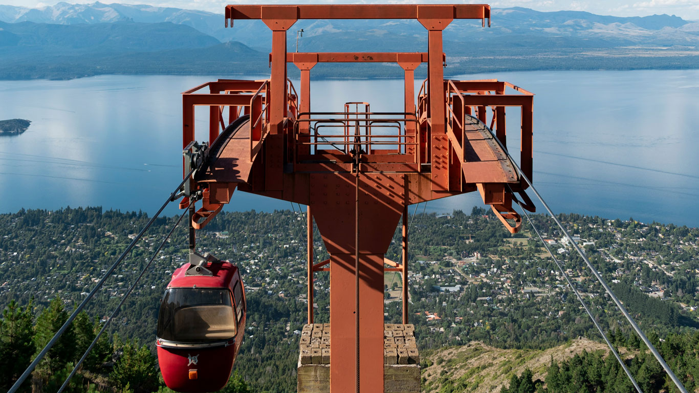 cerro-otto-bariloche Cabina roja del teleférico del Cerro Otto sobrevolando Bariloche, con vistas al lago y las montañas nevadas, una experiencia clásica del invierno en la Patagonia argentina.