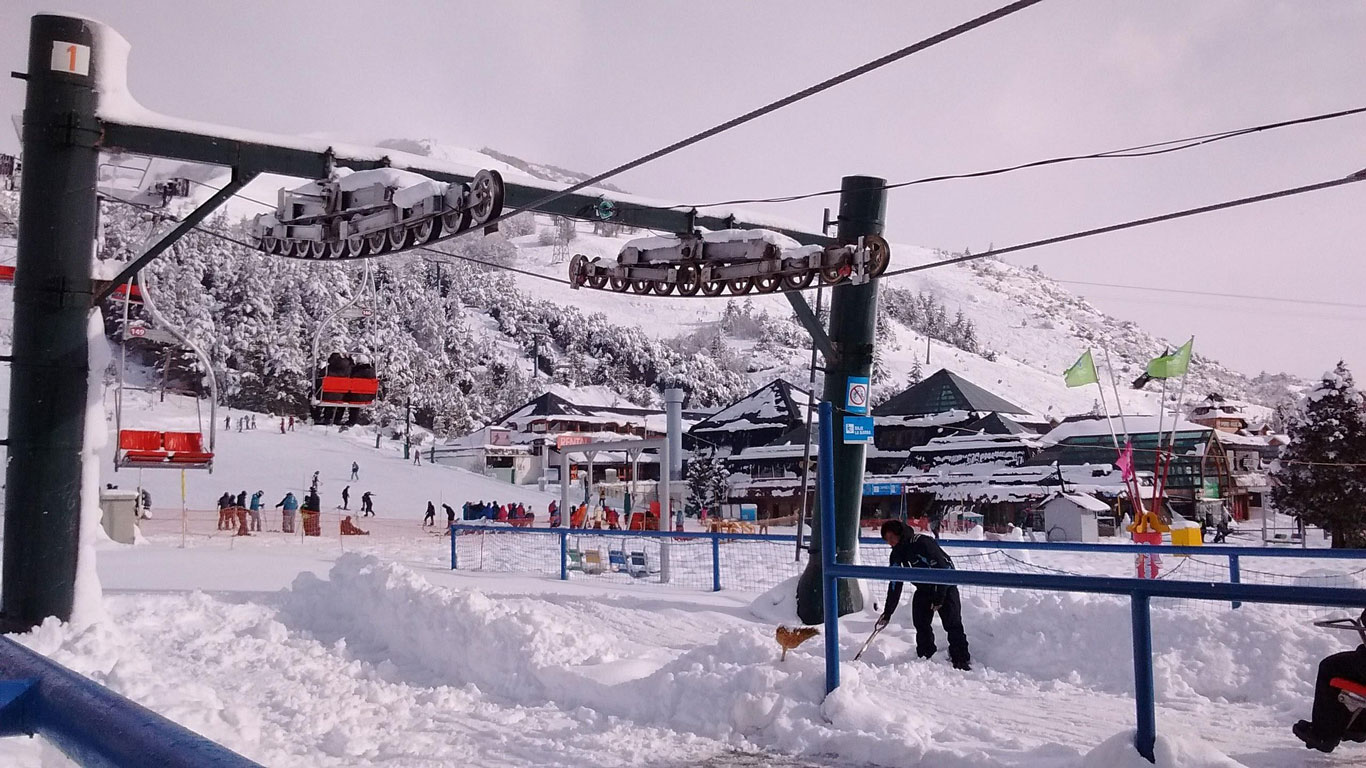 clases-de-ski-en-bariloche Zona base del centro de esquí en Bariloche, llena de actividad con esquiadores, telesillas y nieve fresca, reflejando el ambiente dinámico de la temporada invernal.