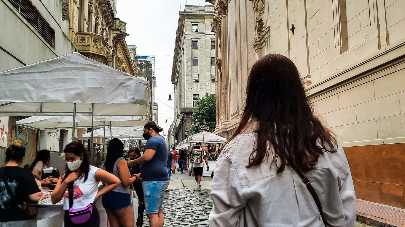 feira-de-san-telmo Mujer caminando por la calle Defensa en San Telmo durante la feria, con puestos blancos a ambos lados y edificios históricos al fondo.