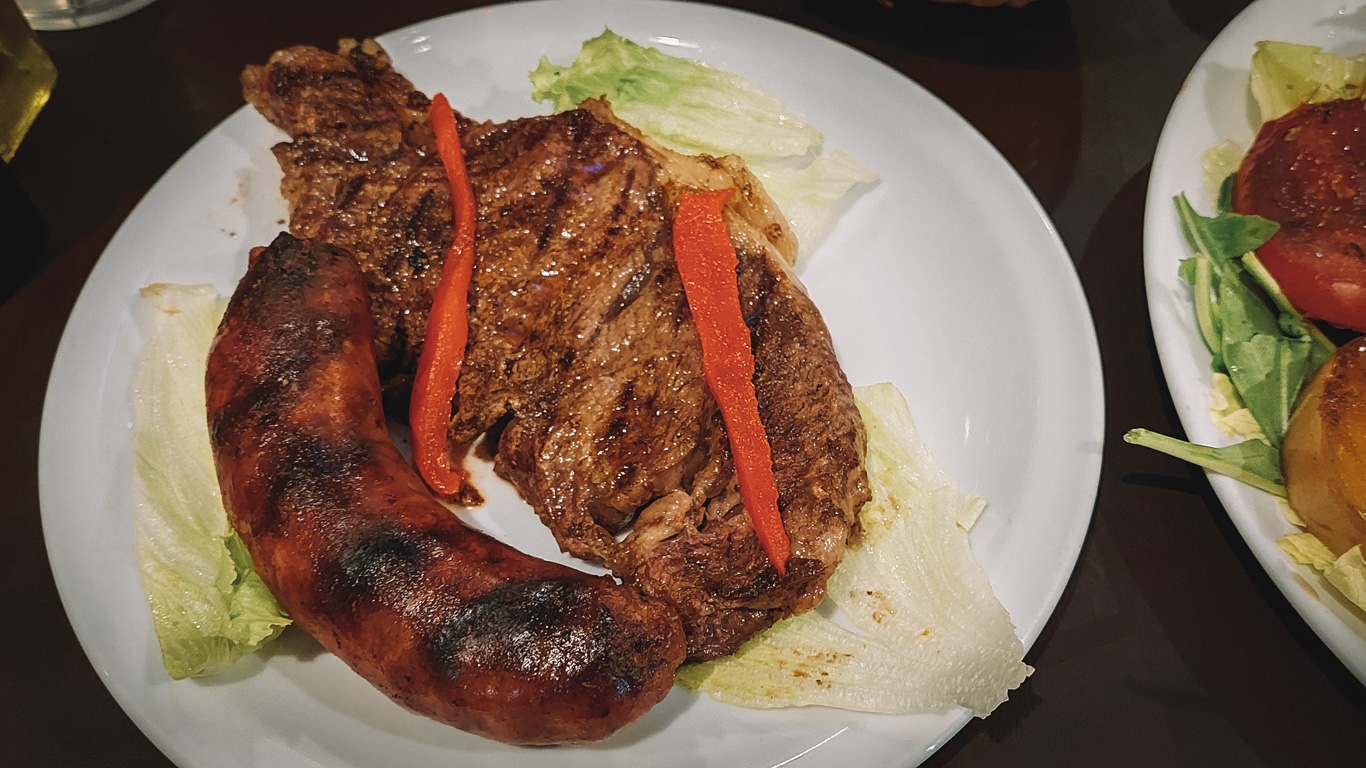 parrilla-argentina Tradicional parrilla argentina, compuesta por un jugoso bife de chorizo y un chorizo, acompañados de hojas verdes y verduras asadas.