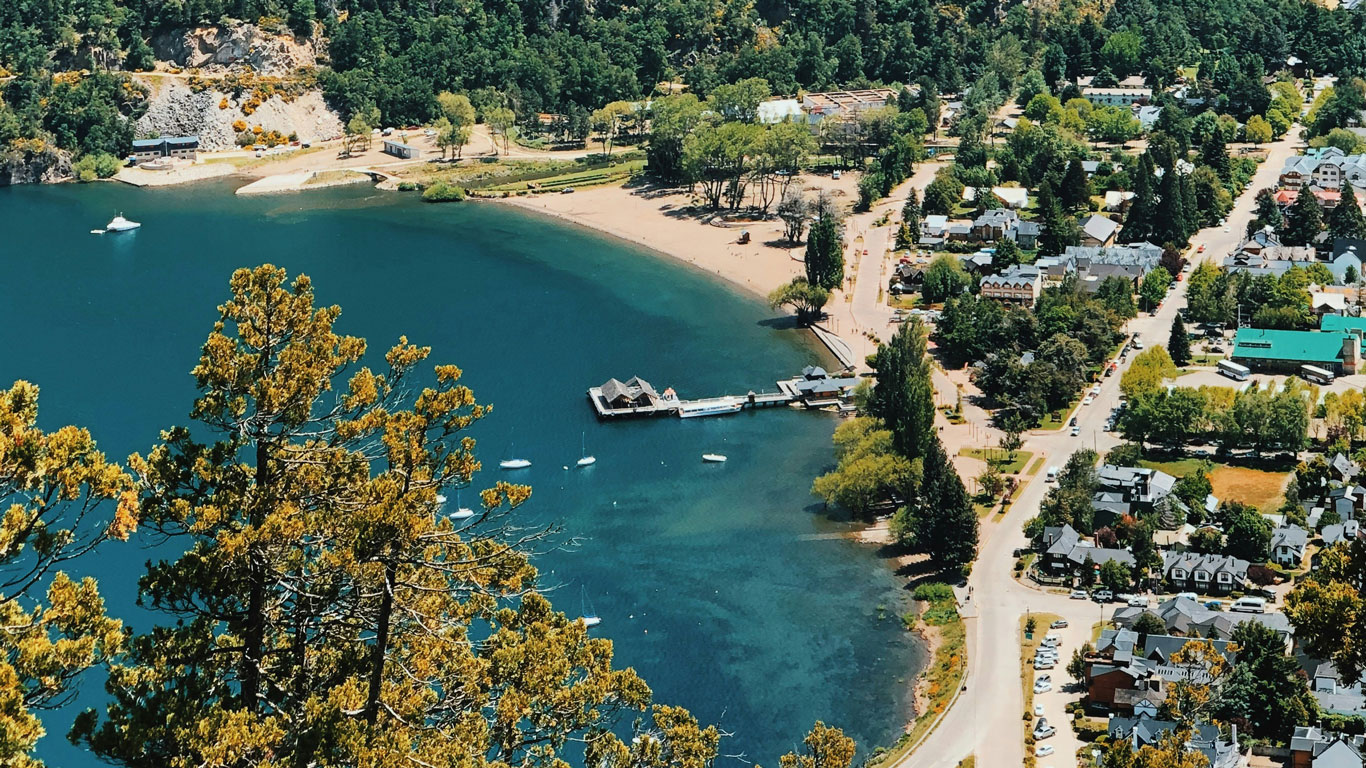 san-martin-de-los-andes Vista panorámica de San Martín de los Andes junto al lago, con muelle y embarcaciones, rodeado de vegetación. Aunque es un destino de verano, en invierno es perfecto para disfrutar de la nieve en Bariloche y sus alrededores.