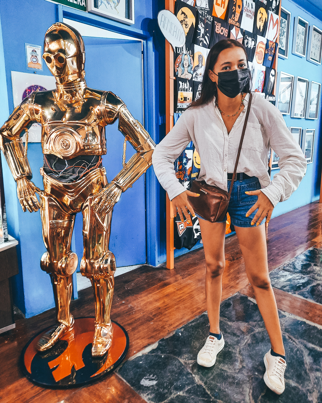 La-Revisteria-Buenos-Aires-1 Una mujer posa imitando la postura de una figura dorada de C-3PO, dentro de una tienda temática decorada con pósteres frikis.