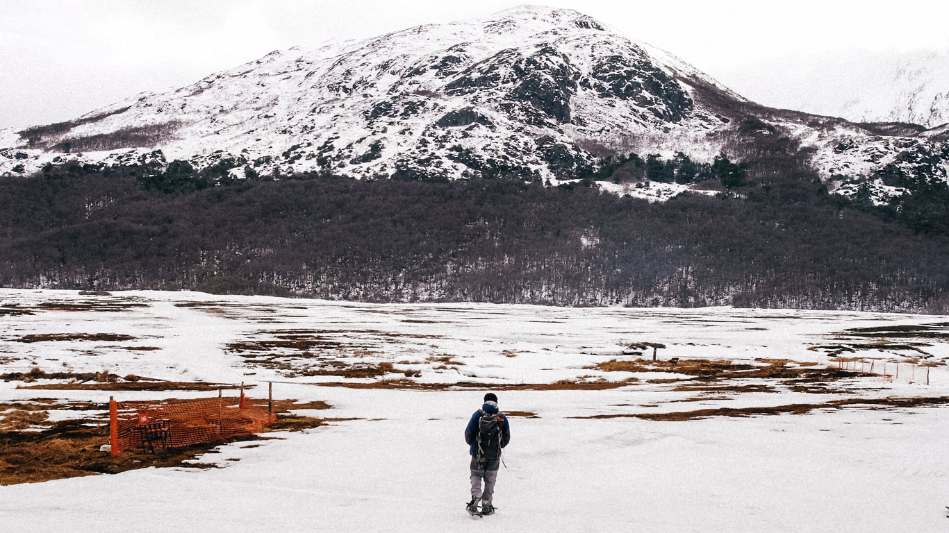 Persona caminando sola sobre la nieve en Ushuaia, con una montaña nevada al fondo, en un paisaje invernal de Tierra del Fuego, Argentina.