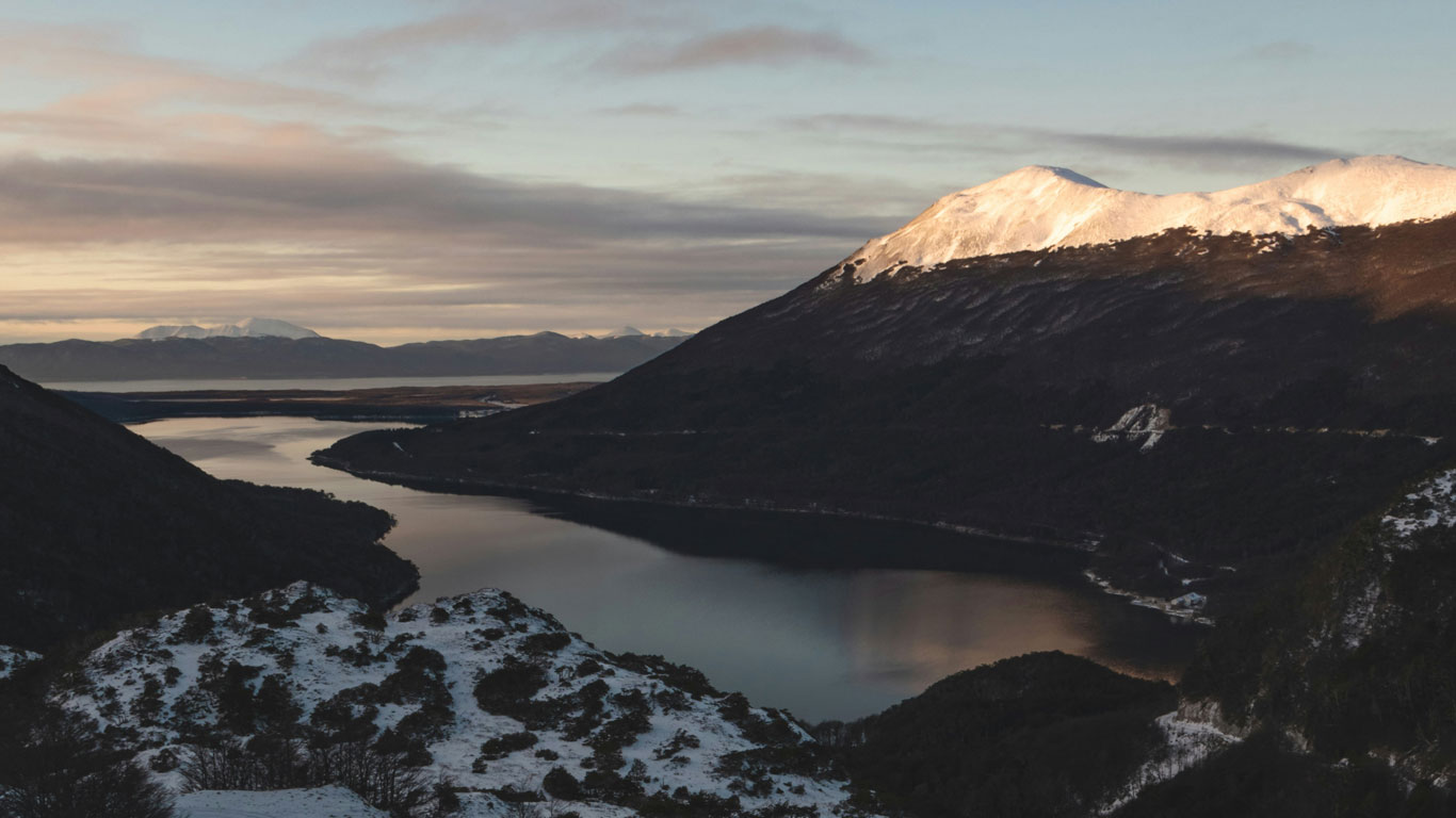 Vista panorámica del Lago Escondido entre montañas cubiertas de nieve en Ushuaia, bajo la luz suave del amanecer.