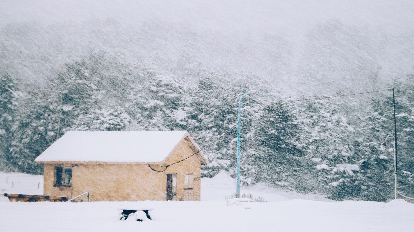 Pequeña casa de campo amarilla en Ushuaia, casi cubierta por una intensa nevada, rodeada de bosque.