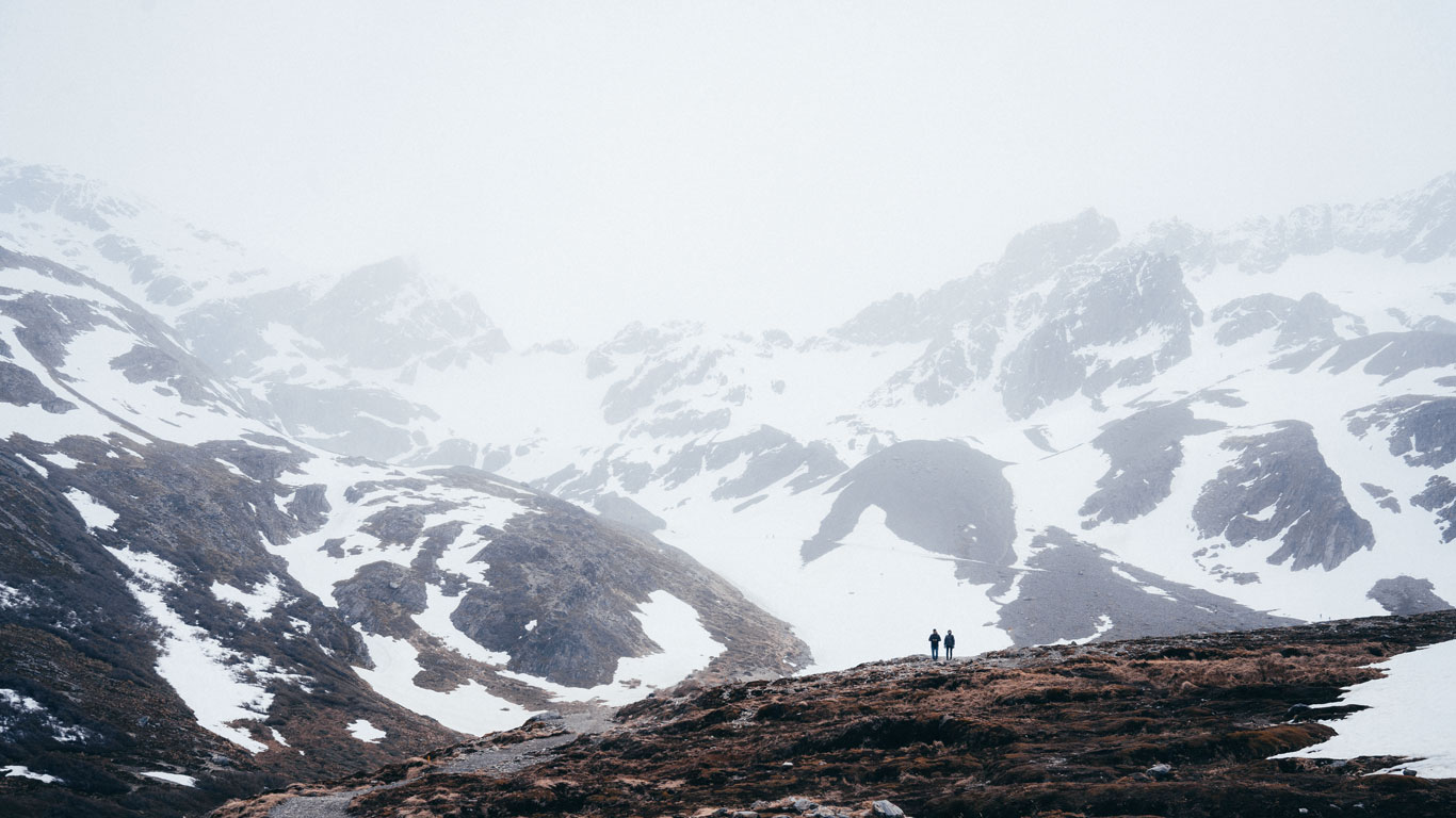Dos personas caminando por un valle entre montañas nevadas bajo una densa niebla en un centro invernal de Ushuaia, creando un ambiente misterioso y aislado.