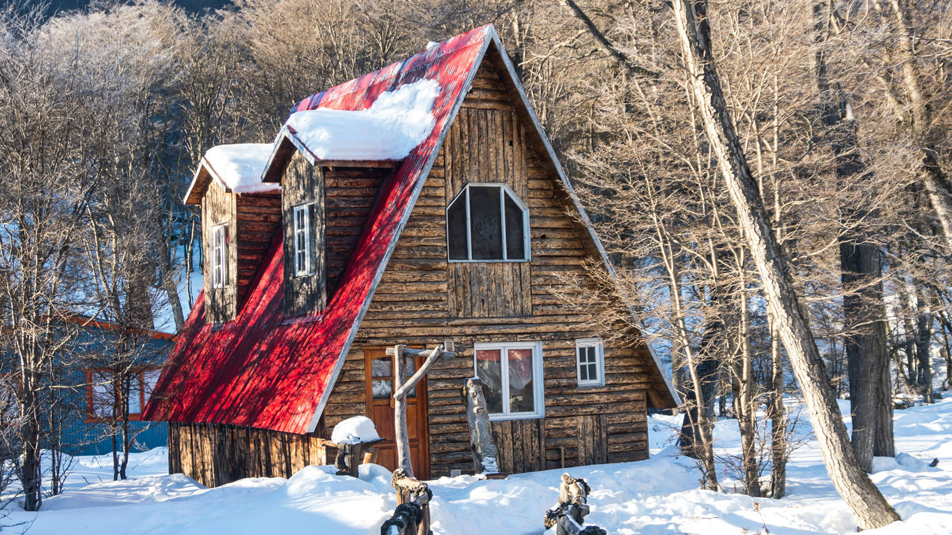 Pequeña casa de campo roja en Ushuaia, con el tejado cubierto de nieve y rodeada de nieve.