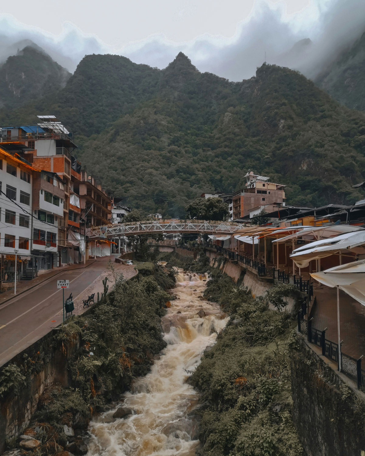 Vista del río que corre entre las construcciones de Aguas Calientes, el mejor lugar para alojarse en Machu Picchu, rodeado de montañas cubiertas de niebla.