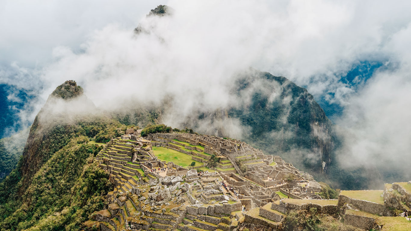 Vista panorámica de las ruinas de Machu Picchu envueltas en niebla y rodeadas de imponentes montañas.