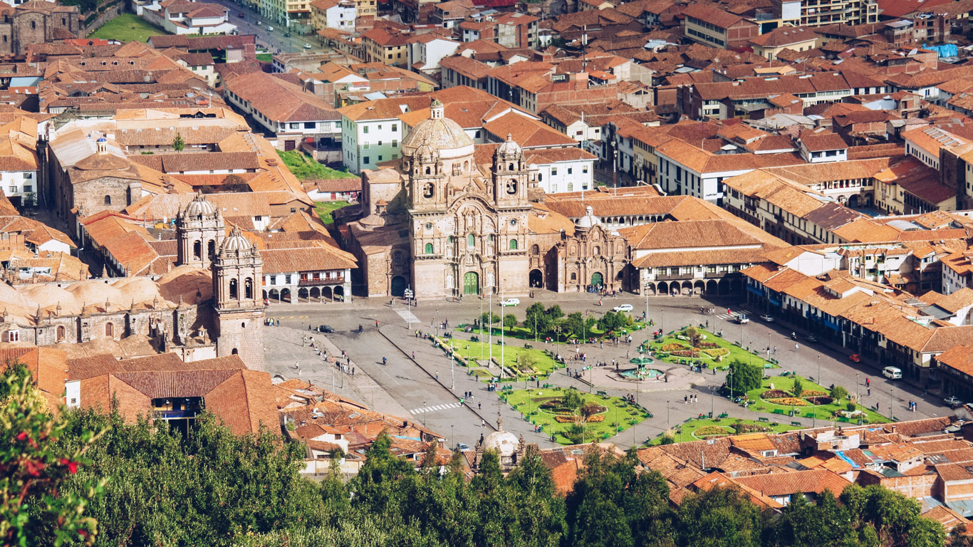 Plaza central de Cusco con la Catedral y personas paseando bajo un cielo parcialmente nublado.