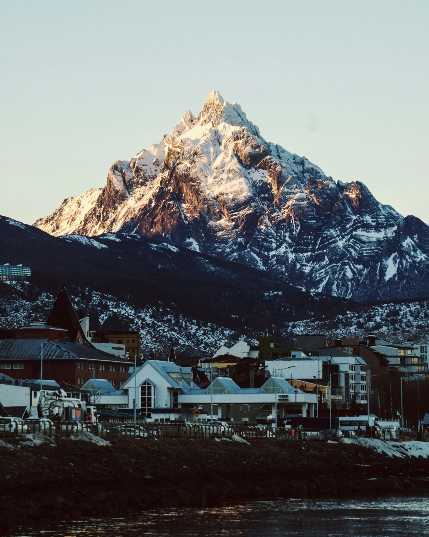 Imagen del centro de Ushuaia con casitas de madera y montañas nevadas al fondo.