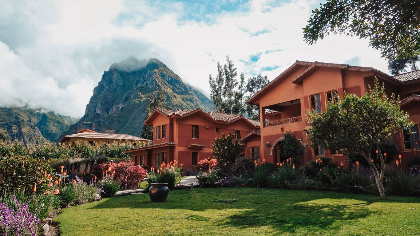 Hotel boutique en el Valle Sagrado con jardines floridos y montañas al fondo, bajo un cielo azul.