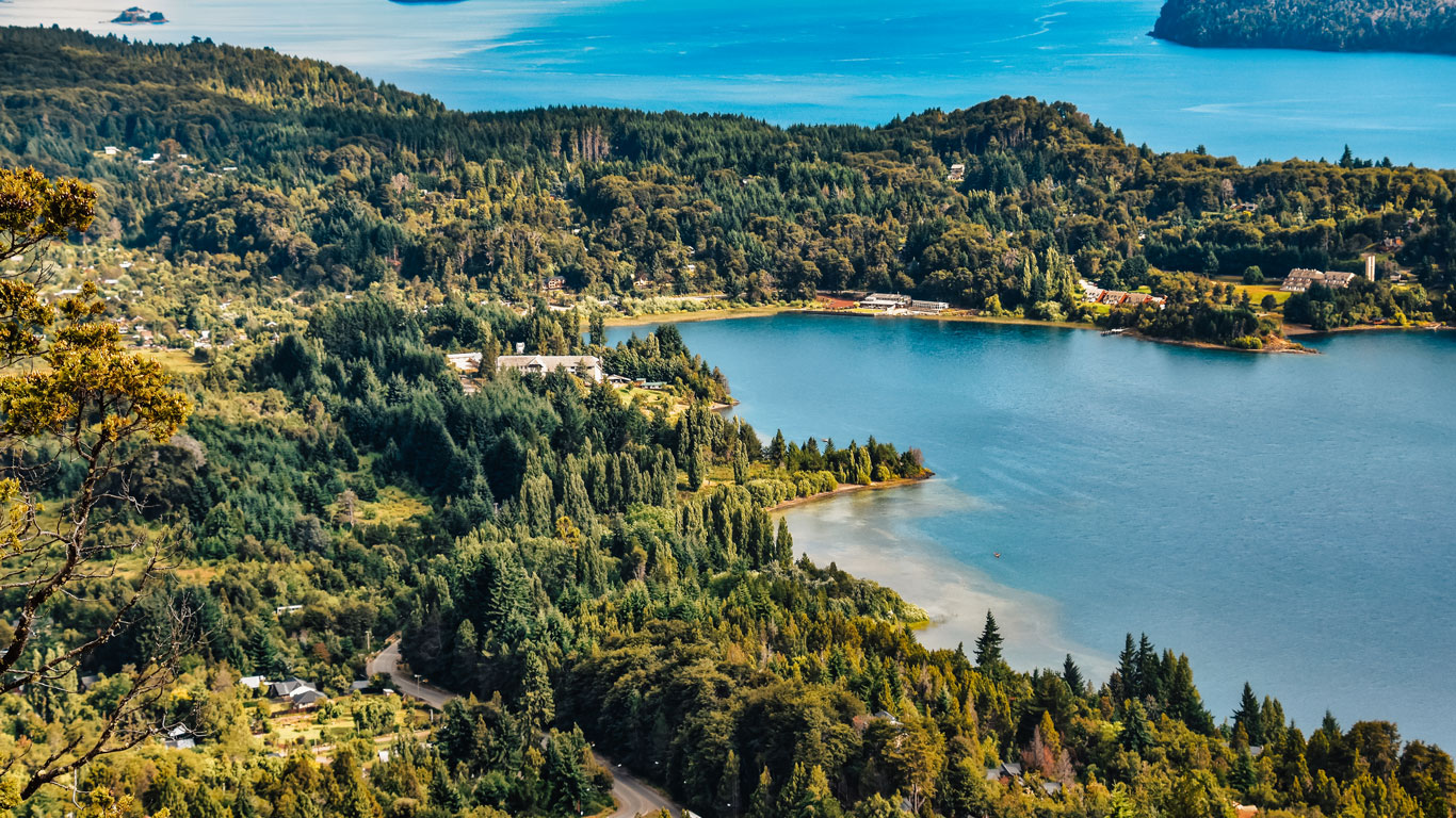 Vista panorámica del Lago Nahuel Huapi en Bariloche, rodeado de bosques densos y pequeñas construcciones dispersas.
