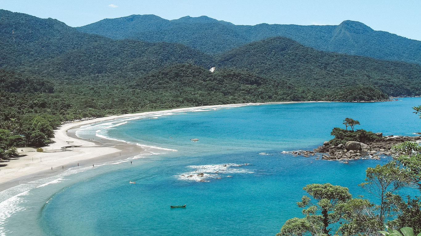 Praia de Castelhanos, la playa más aislada dónde alojarse en Ilhabela, vista desde un mirador en un día soleado. El mar azul cristalino y su costa en forma de corazón, completamente rodeada por la Mata Atlántica, crean una de las postales más impresionantes de la isla.