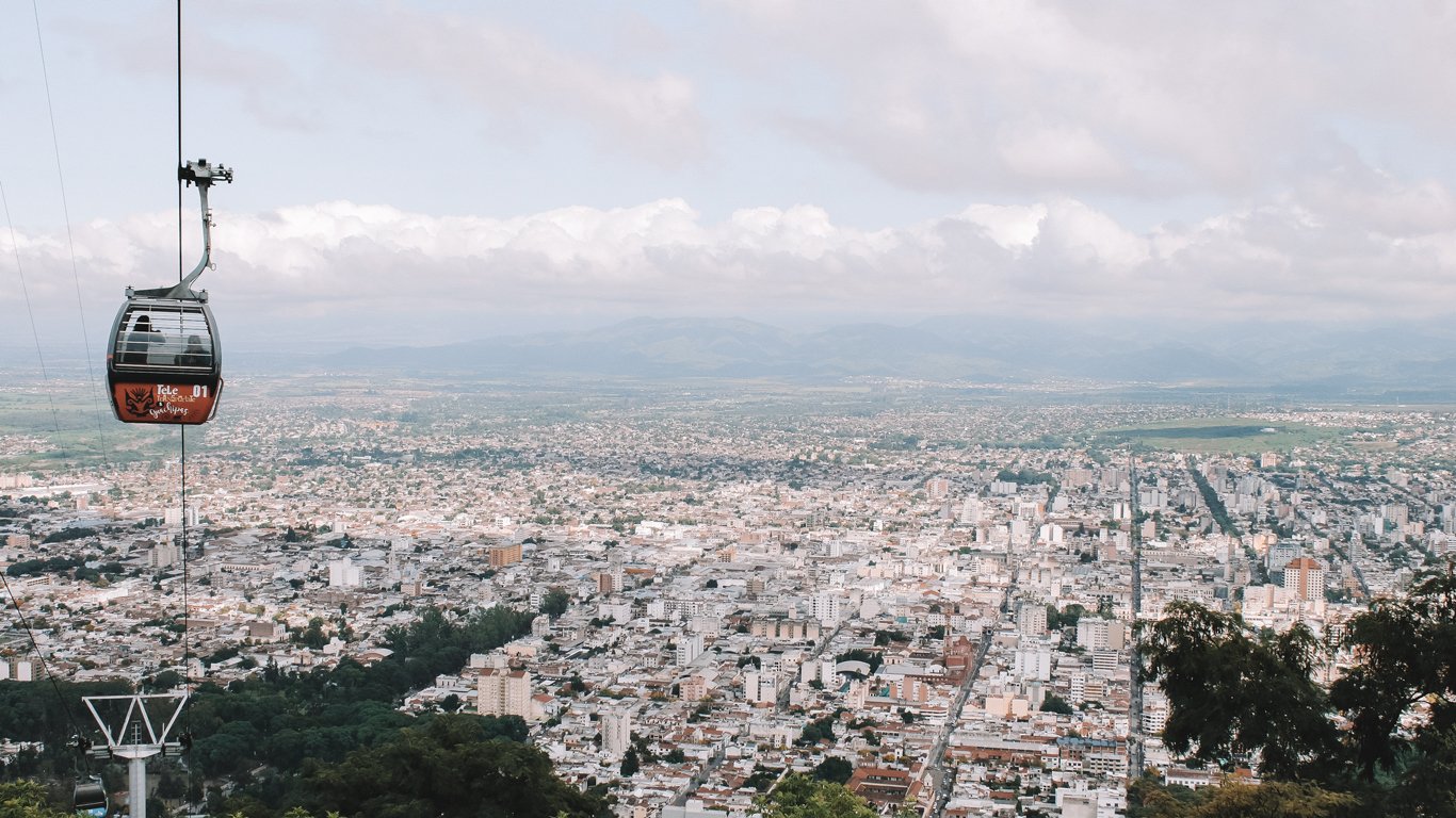 Salta vista desde un mirador con un teleférico en primer plano. La ciudad se mezcla con el cielo ligeramente nublado en el horizonte.